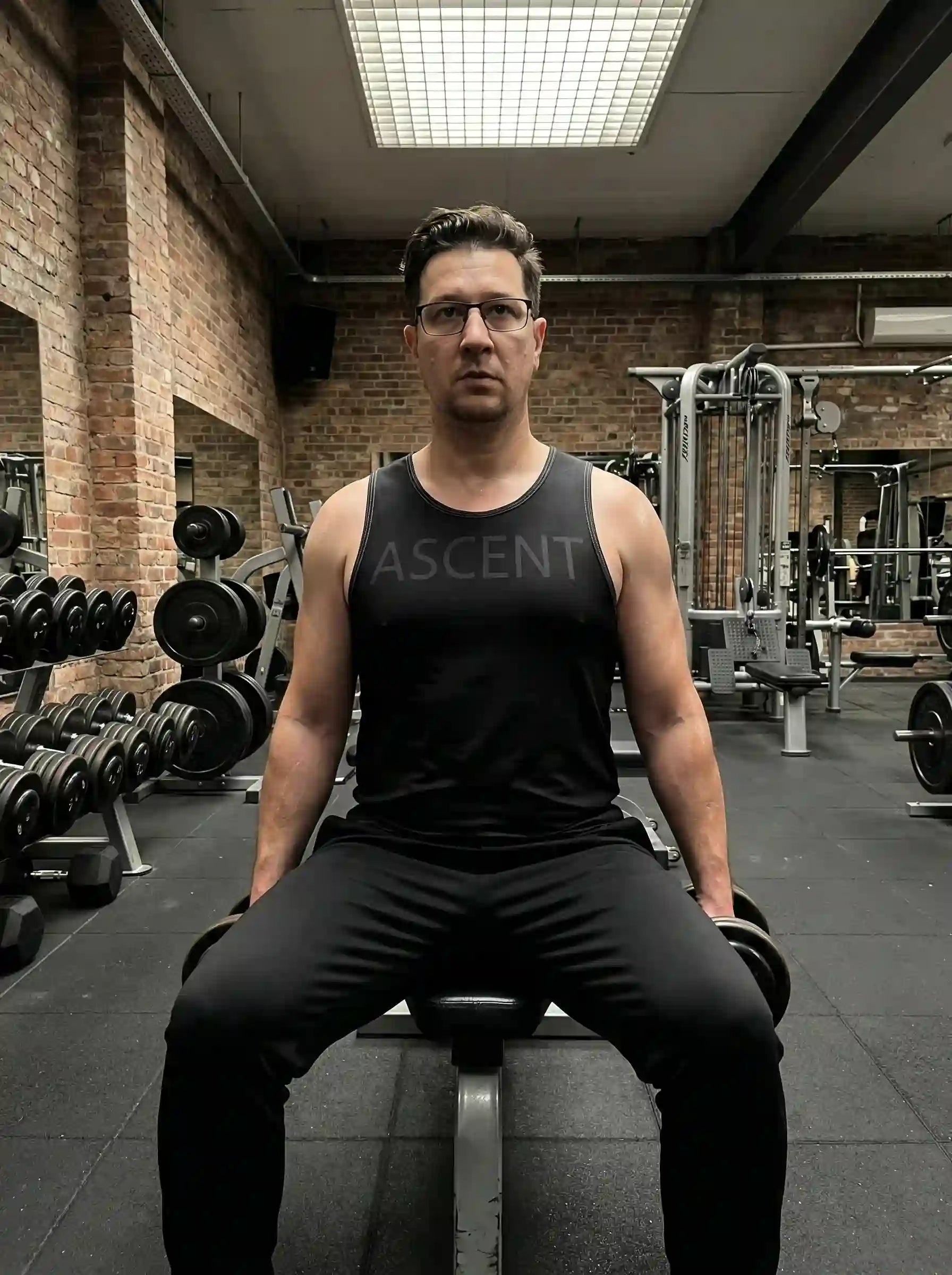 Homme assis sur un banc réalisant un row avec haltères, portant le debardeur ASCENT — Training.